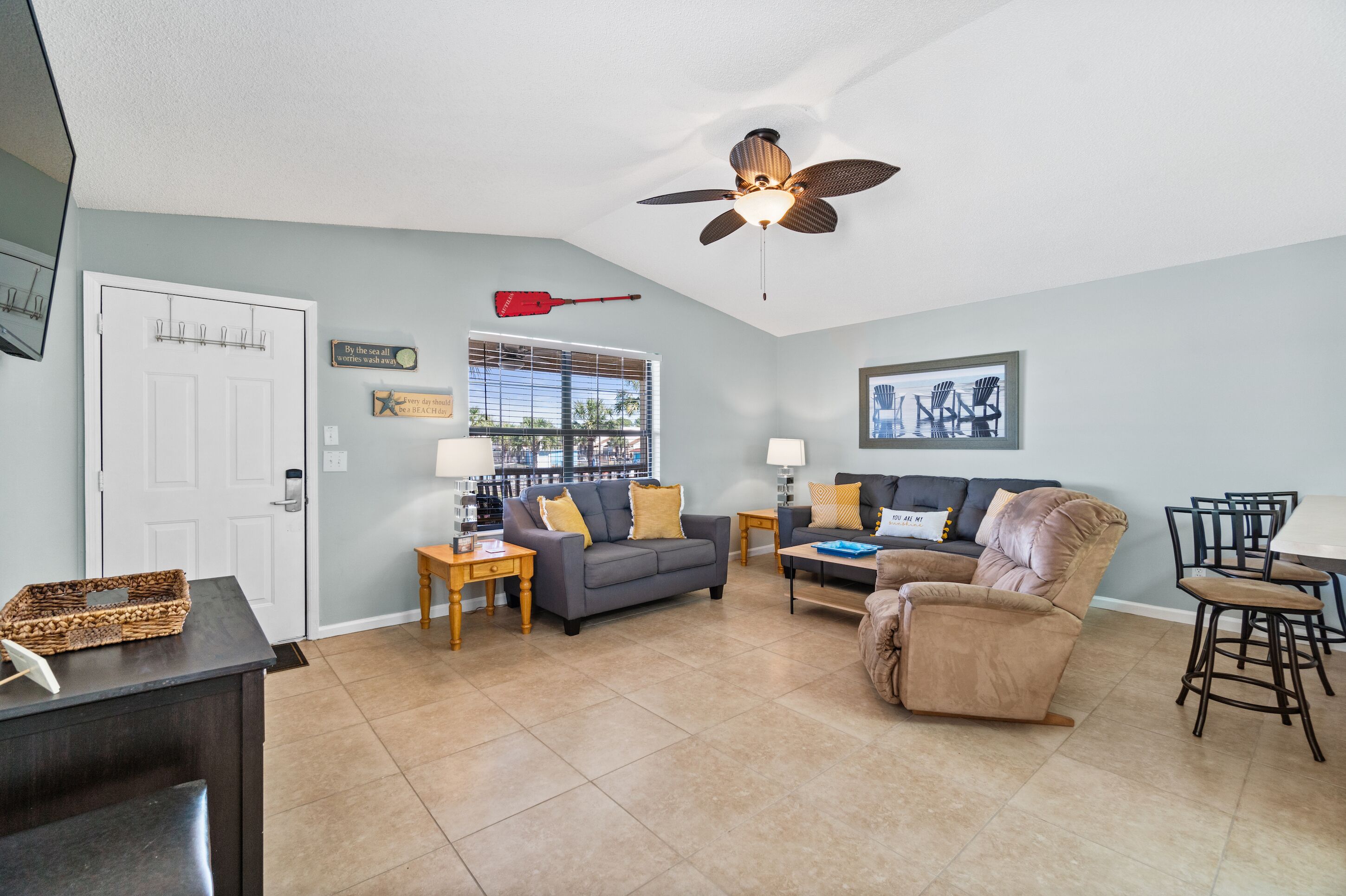 A living room with a ceiling fan, a gray sofa, a brown armchair, a coffee table, and a dining area with a table and chairs.