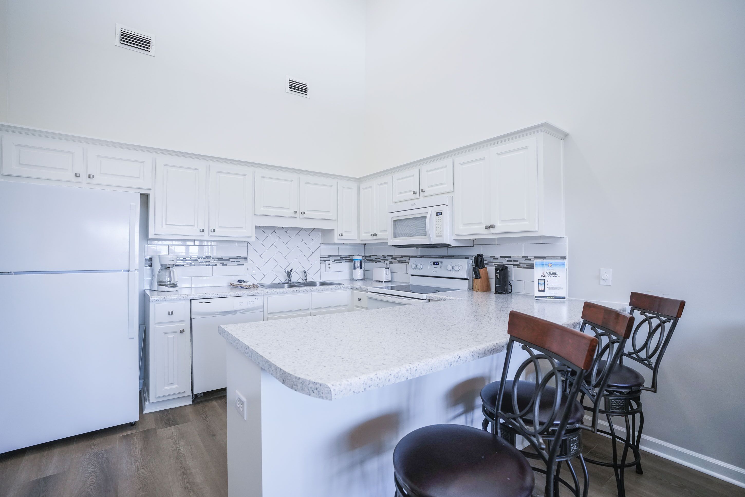A modern kitchen with white cabinetry, a granite countertop, and a central island with bar stools.