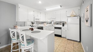 Een moderne keuken met witte kasten, een centraal eiland met stoelen, een koelkast en een magnetron.