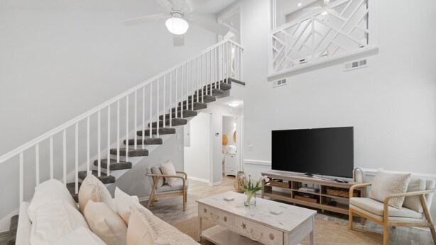Een ruime woonkamer met een trap, een flatscreen televisie en een comfortabele zithoek.