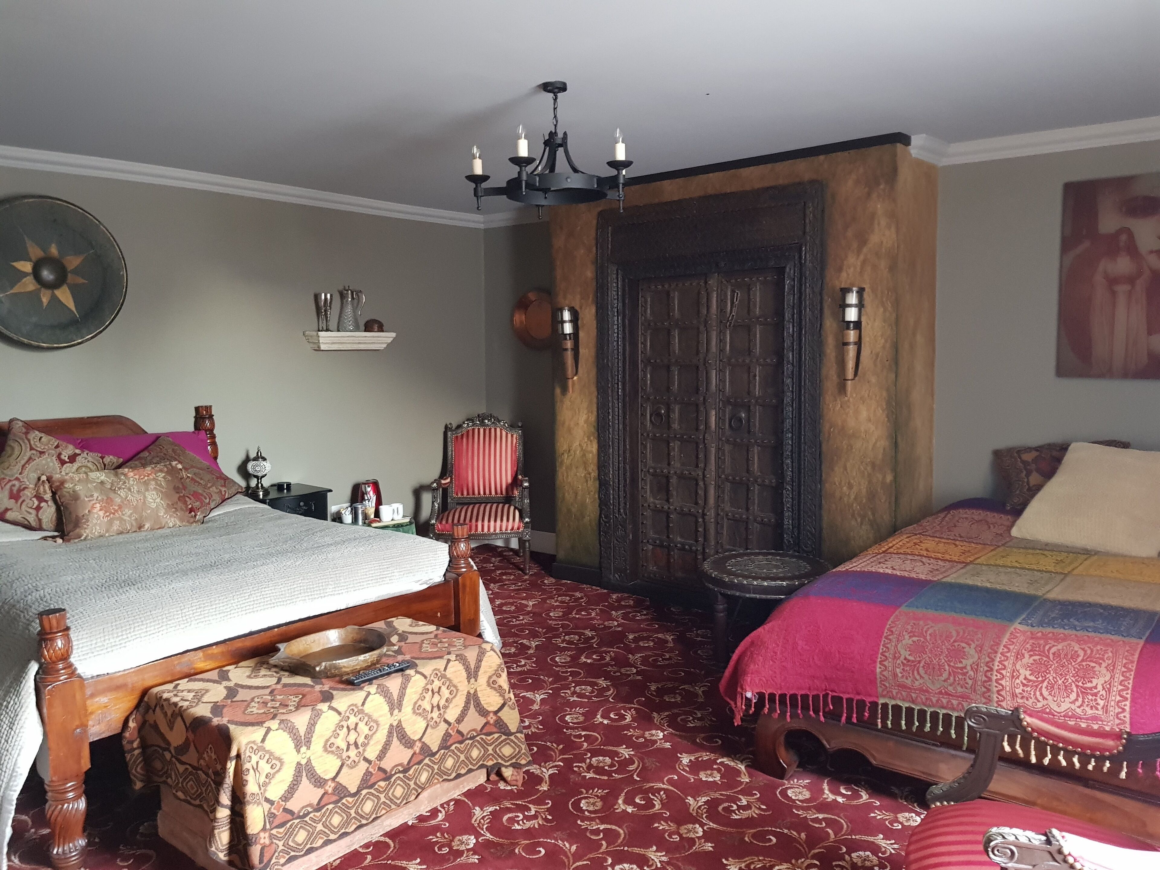 A bedroom with two beds, a chandelier, a wooden door, and a patterned carpet.