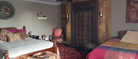 A bedroom with two beds, a chandelier, a wooden door, and a patterned carpet.
