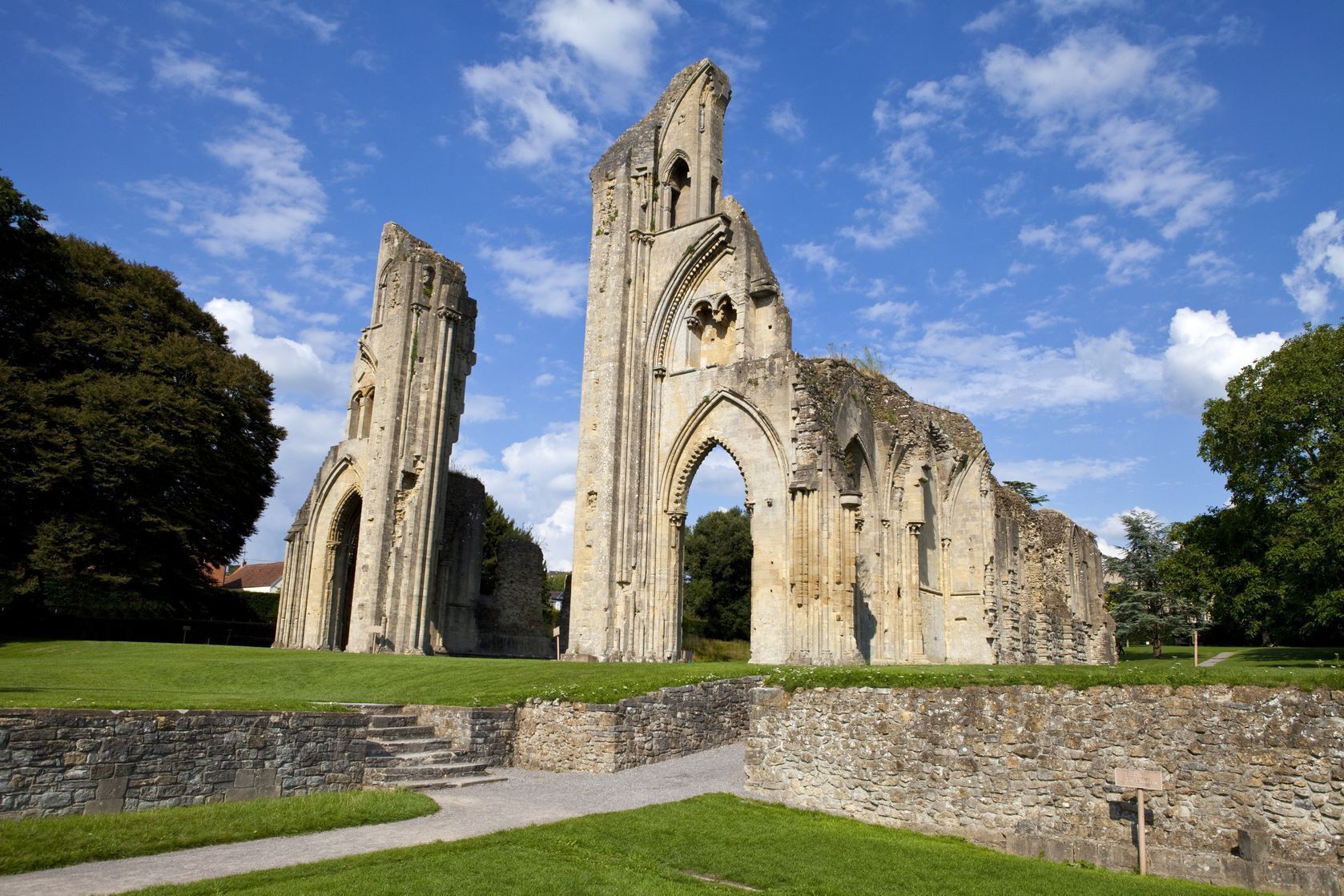 A historic stone structure with arches and columns, surrounded by a grassy area and trees.