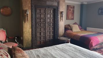Una camera da letto con un'ampia porta in legno, un letto con biancheria a motivi, uno sgabello e una sedia con cuscini rossi.