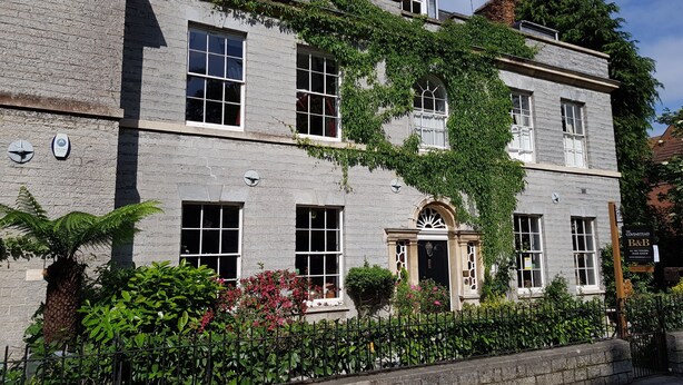 A two-story building with a stone facade, multiple windows, and a central entrance with a decorative arch. - The Covenstead (Glastonbury)
