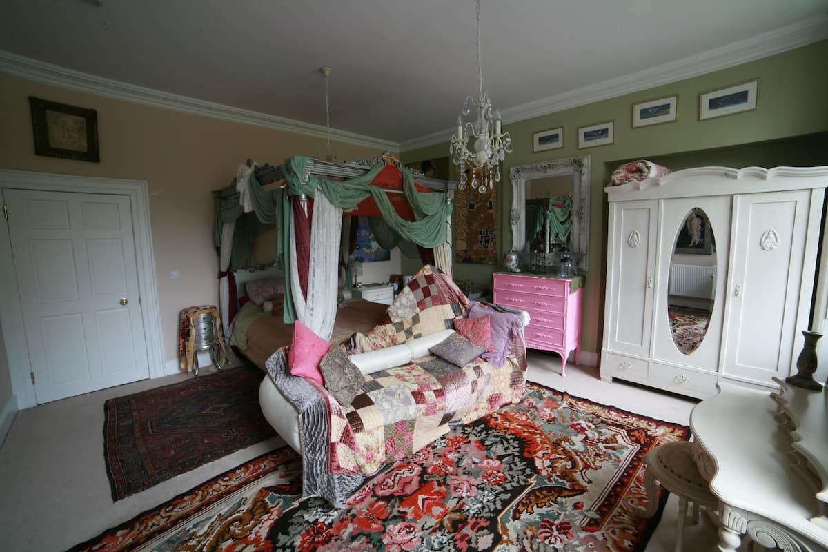 A bedroom with a four-poster bed, a chandelier, a dresser, and a mirror.