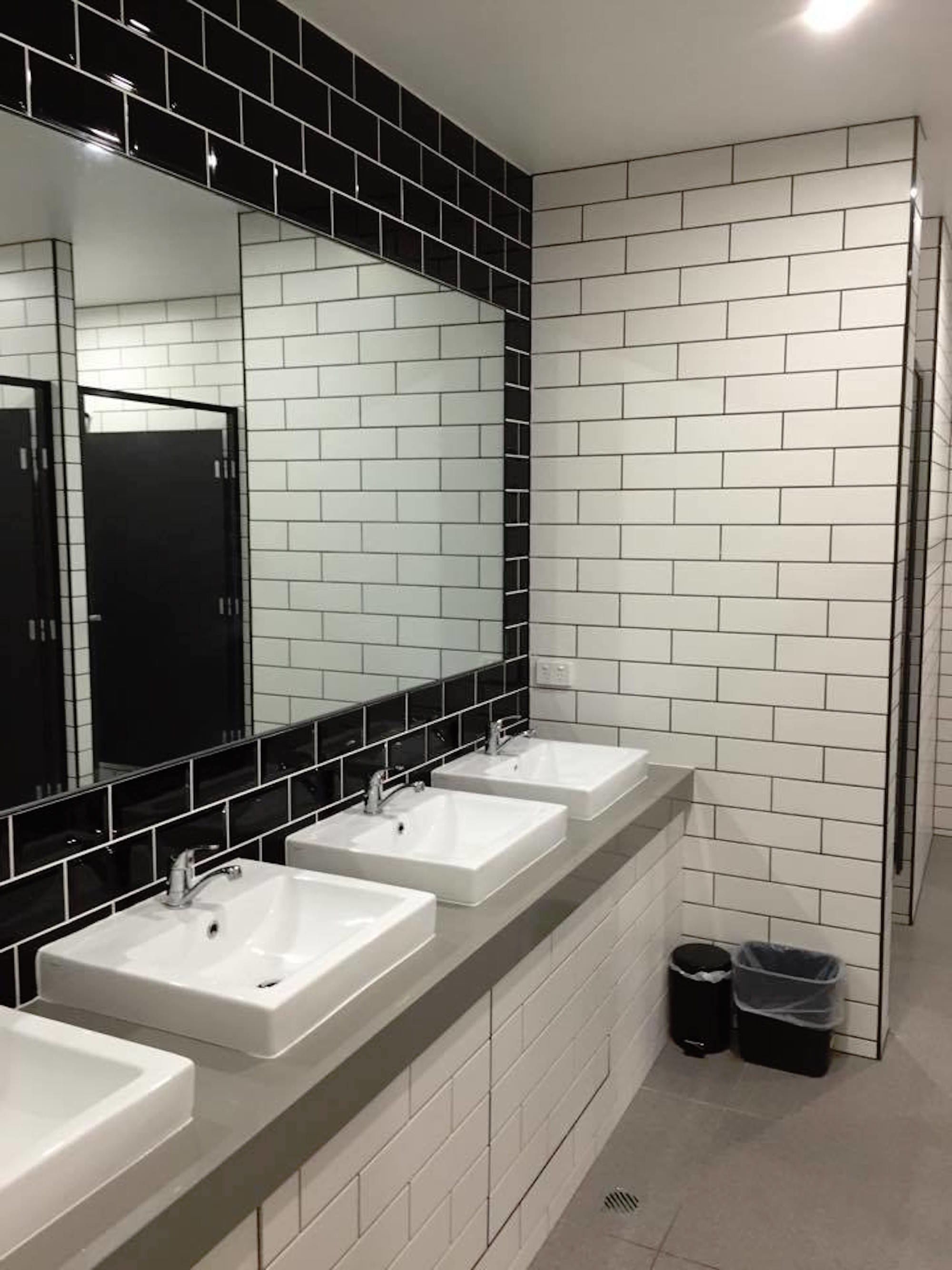 A modern bathroom with three white sinks, black tiled walls, and a large mirror.