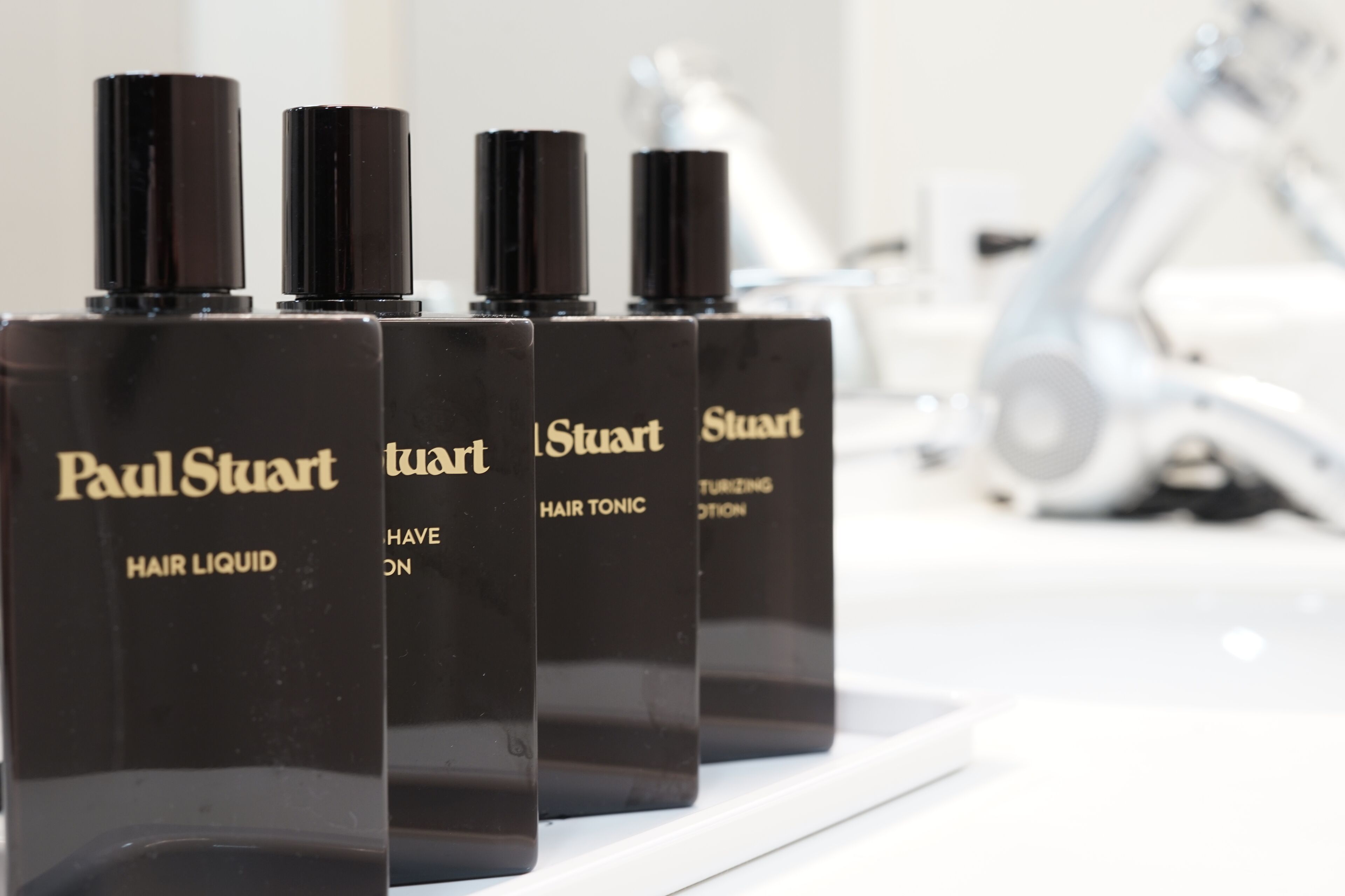 Four bottles of Paul Stuart hair liquid on a white shelf.