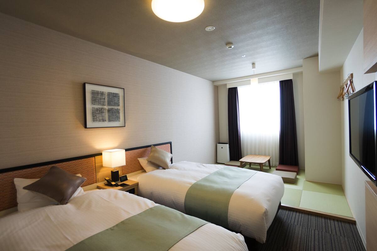 Een hotelkamer met twee bedden, een bureau, een stoel, een televisie en een raam met gordijnen.