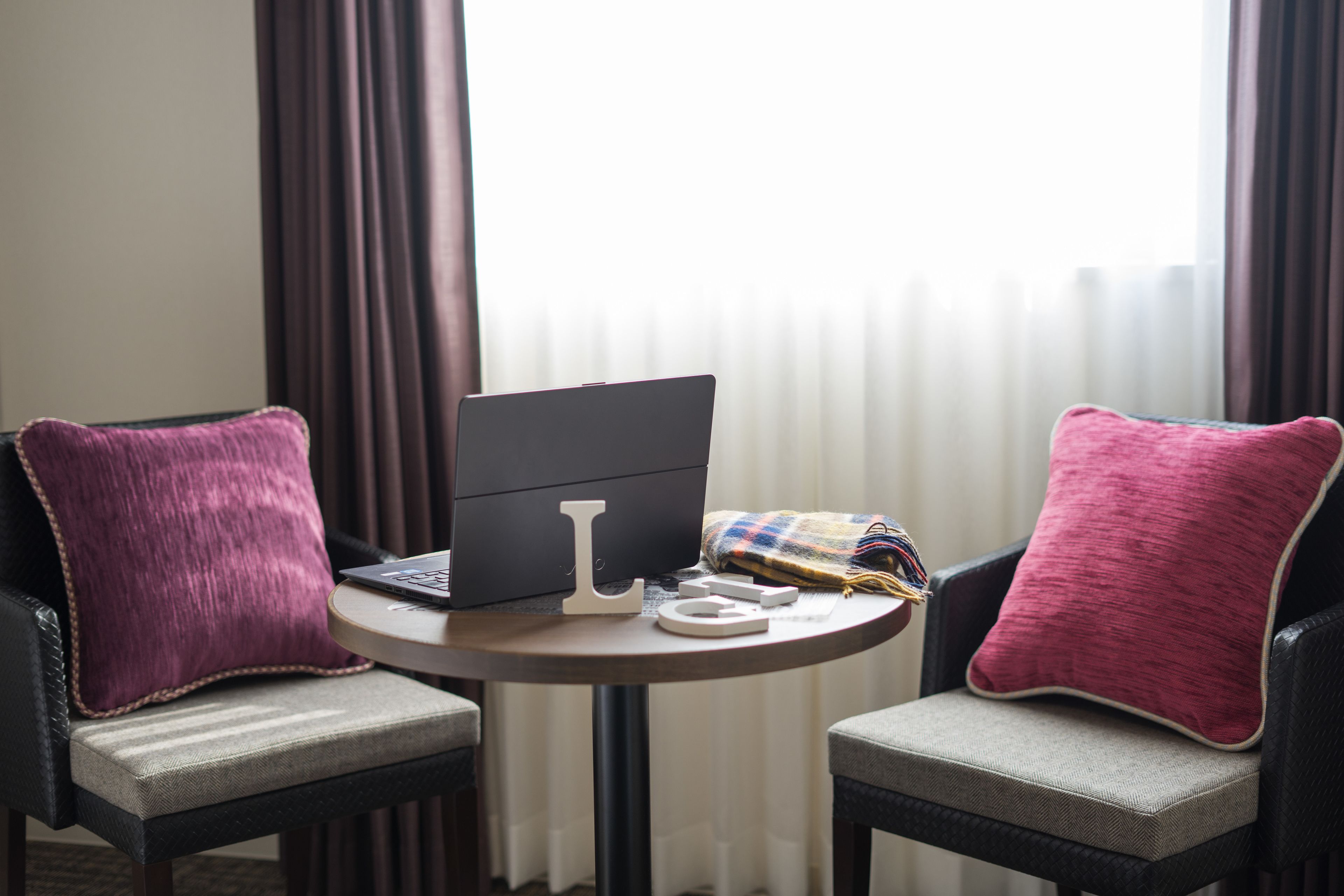 Habitación de hotel con dos sillones, una mesita redonda con una computadora portátil y una manta.