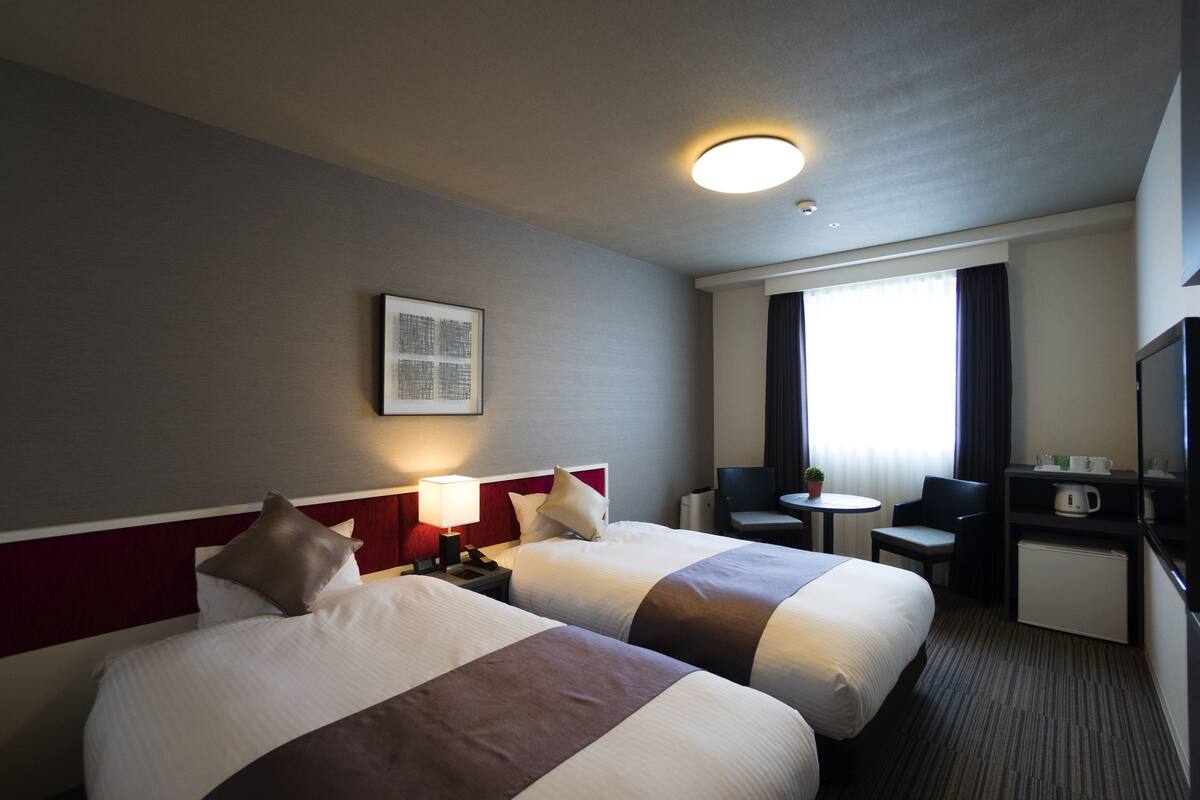 Een hotelkamer met twee bedden, een bureau, een stoel, een klein tafeltje en een televisie.