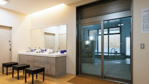A modern bathroom with a large mirror, a sink with toiletries, and two stools.