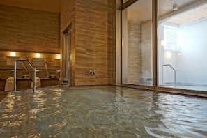 Zona de spa con jacuzzi, paredes de madera y puerta de vidrio que da al exterior.