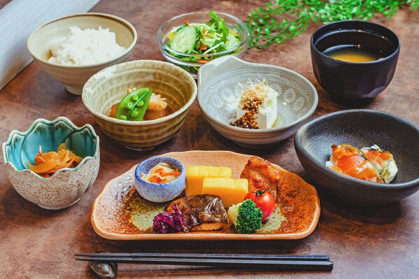 Diversos platos que incluyen arroz, verduras y carne, servidos sobre una mesa de madera con palillos.