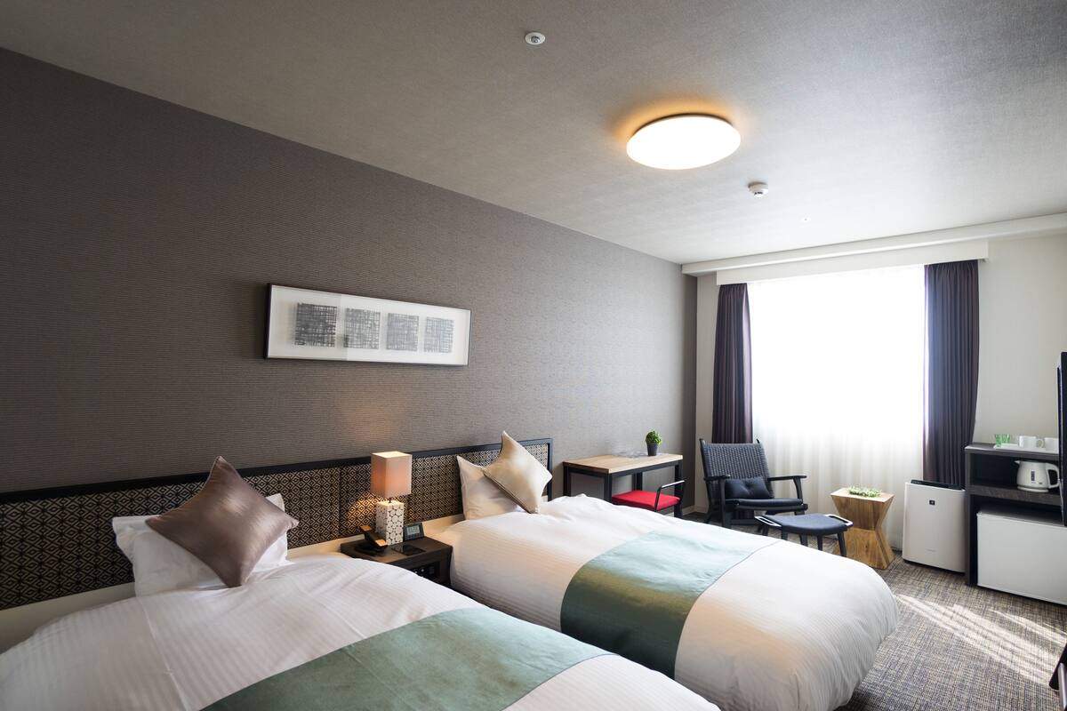 Een hotelkamer met twee bedden, een bureau, een stoel, een kleine tafel en een televisie.