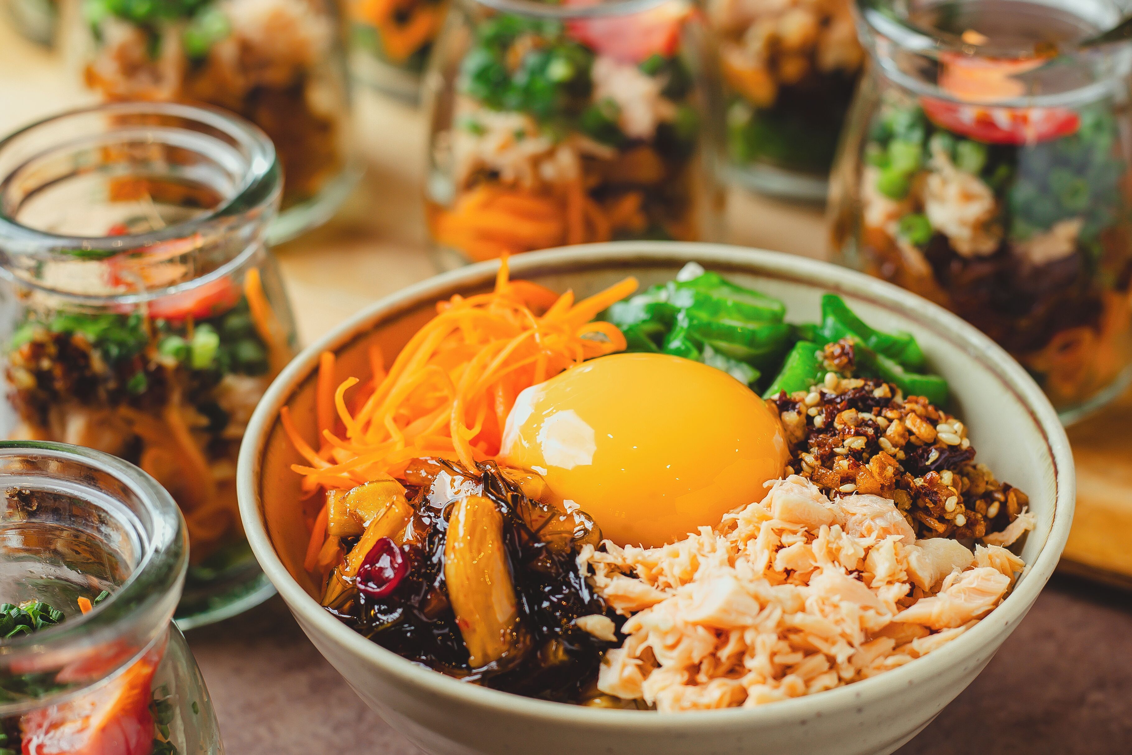 A bowl of food with various ingredients including shredded carrots, greens, and a boiled egg.