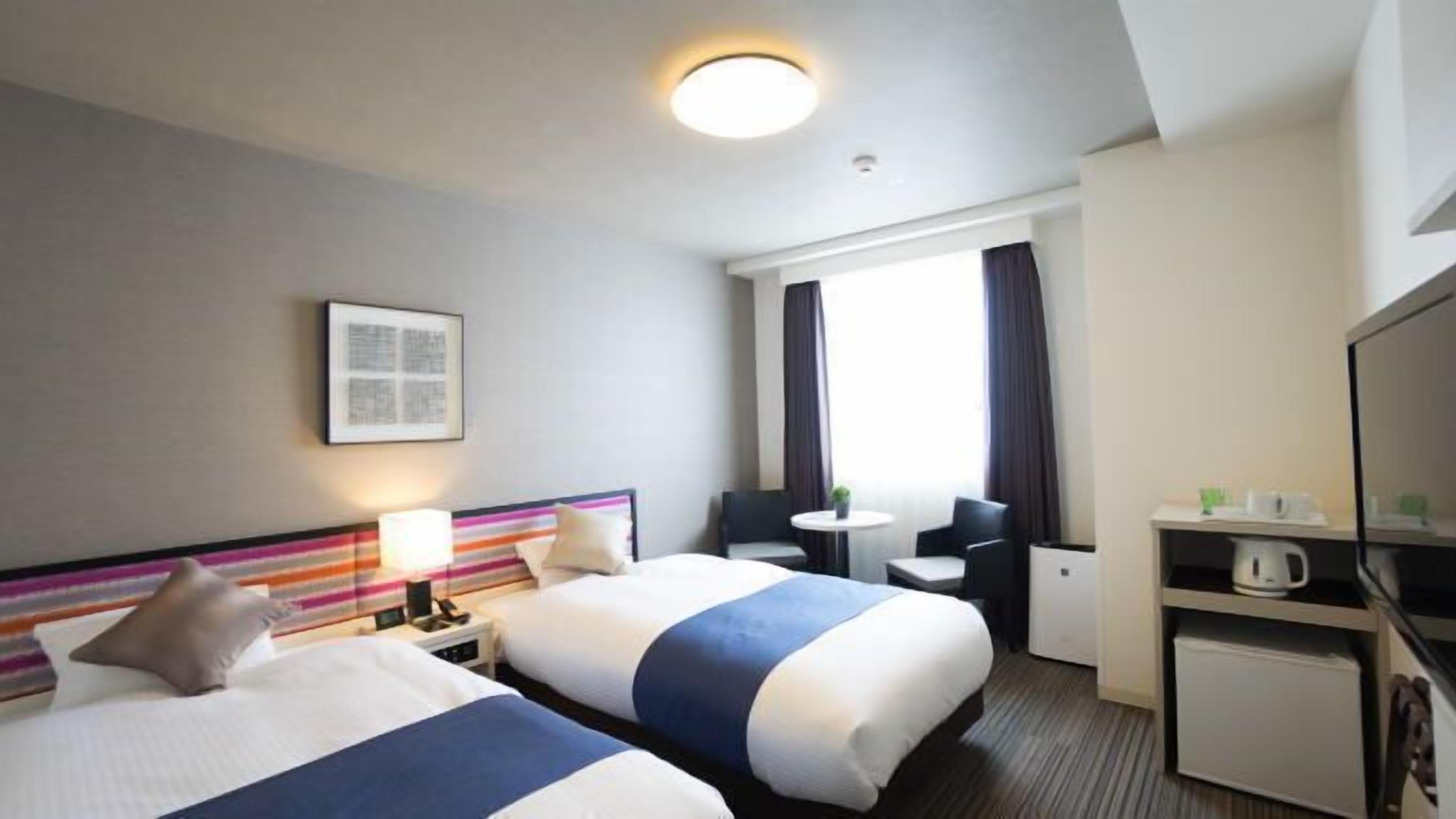 Une chambre d’hôtel avec deux lits, un bureau, une chaise, une télévision et une fenêtre avec des rideaux.