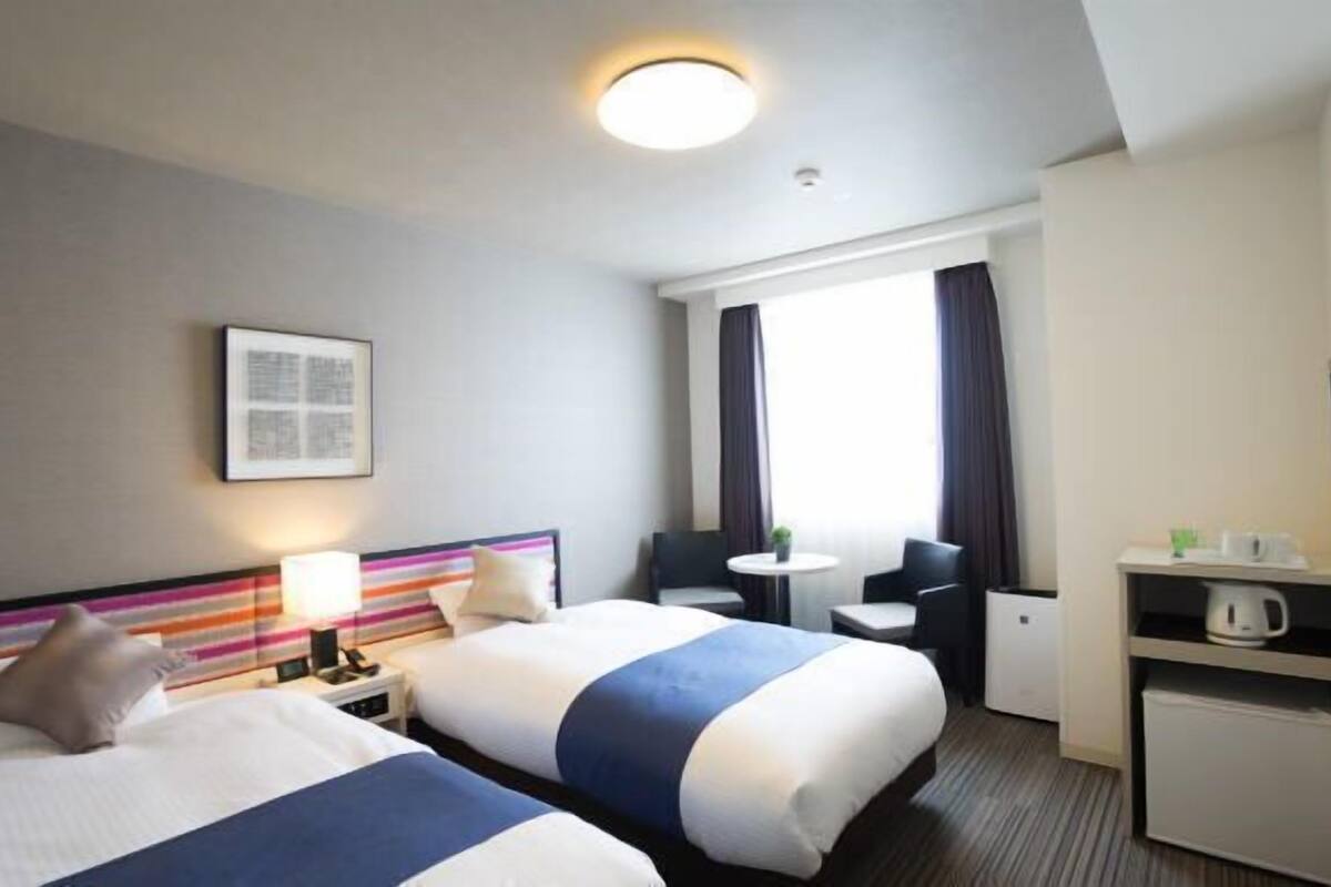 Een hotelkamer met twee bedden, een bureau, een stoel, een televisie en een raam met gordijnen.