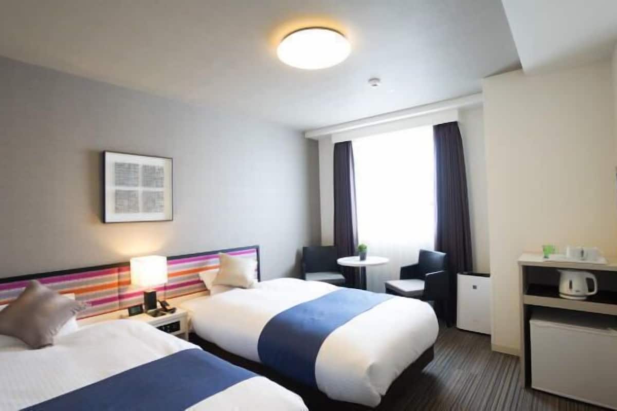 A hotel room with two beds, a desk, a chair, a TV, and a window with curtains.