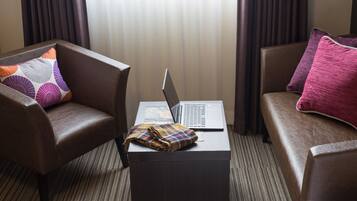 Et hotelværelse med to brune lædersofaer, hvoraf den ene har en pude med lilla og orange mønster, og en bærbar computer på et lille bord imellem dem.