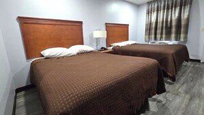 A hotel room with two beds, a nightstand, a lamp, and a window with curtains.