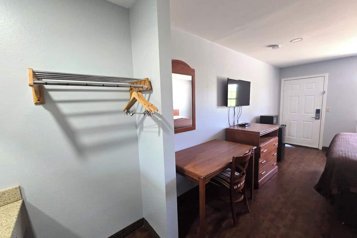 A hotel room with a wooden desk, a TV, a wardrobe, and a bed.
