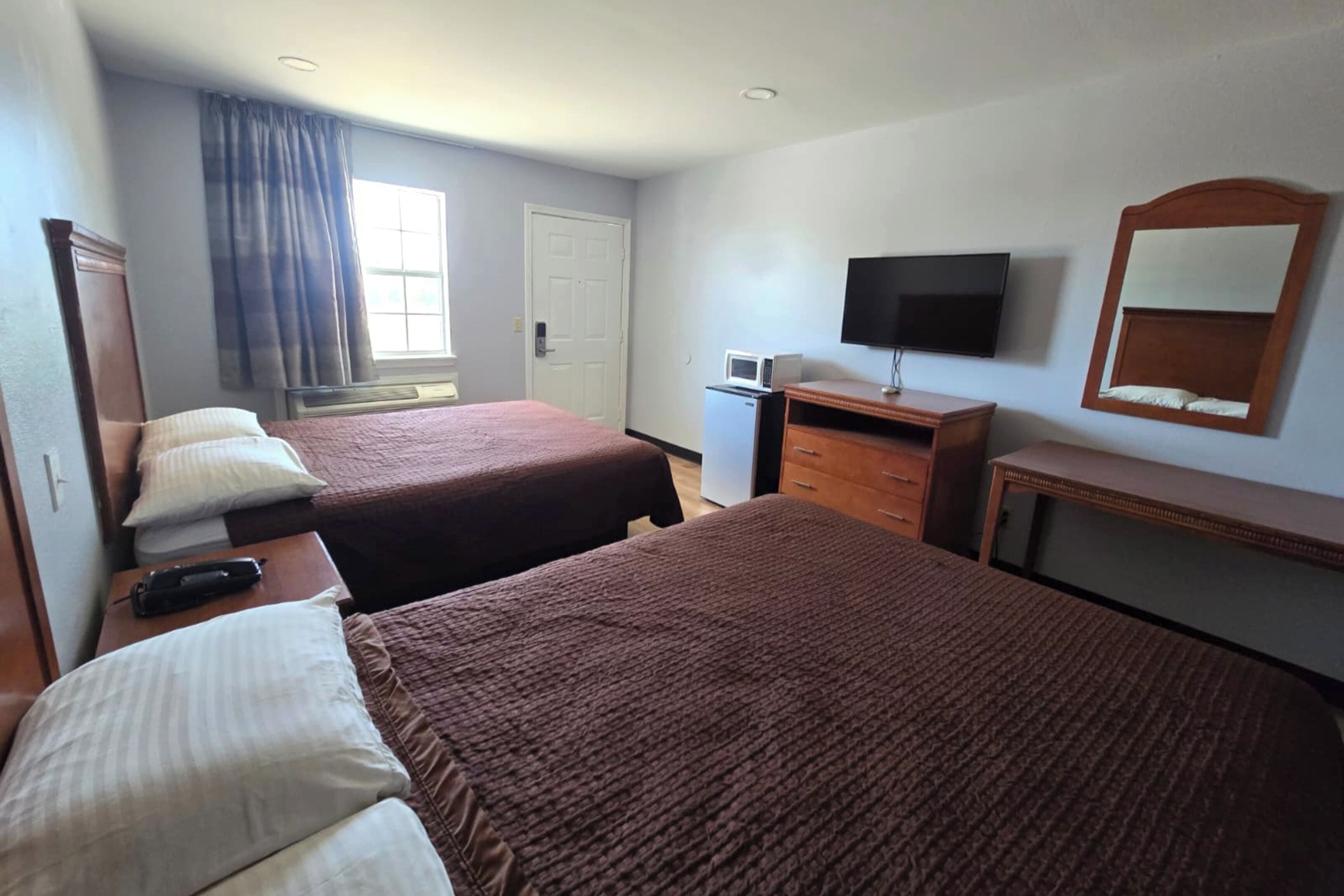 A hotel room with two beds, a TV, a desk, and a window with curtains.
