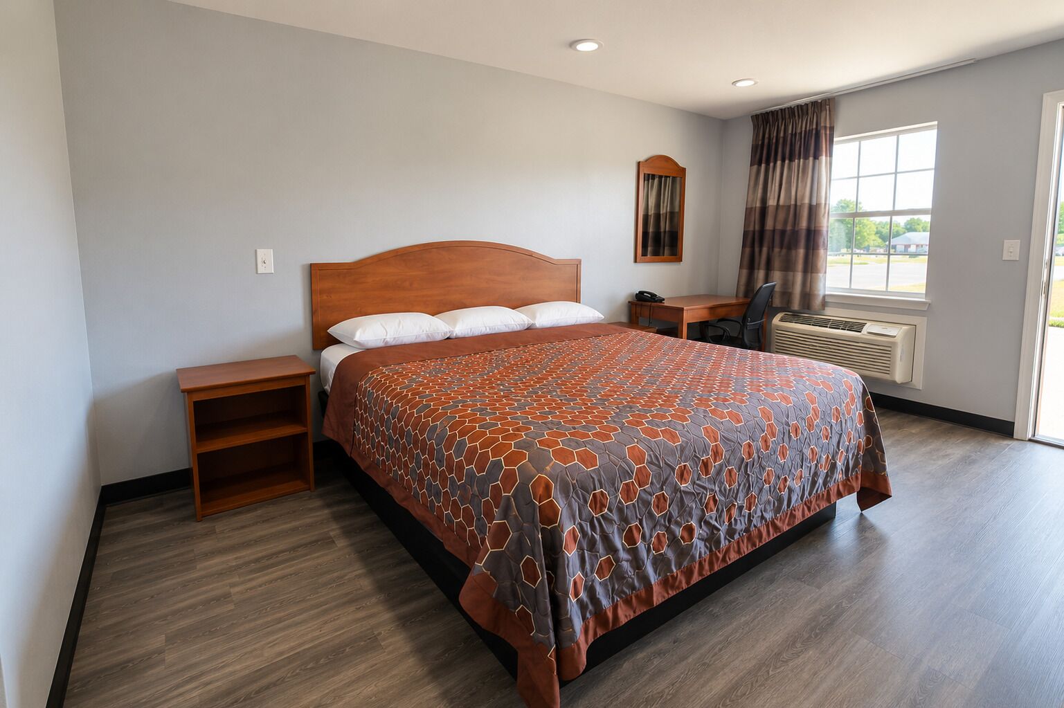 Une chambre d’hôtel avec un grand lit, un bureau, une chaise, un téléphone et une fenêtre avec des rideaux.
