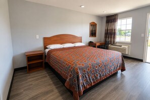 Habitación de hotel con una cama grande, un escritorio, una silla, un teléfono y una ventana con cortinas.