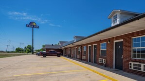 A Stay Inn with a parking lot, a maroon SUV, and a brick building with multiple windows.