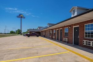 A Stay Inn with a parking lot, a maroon SUV, and a brick building with multiple windows.