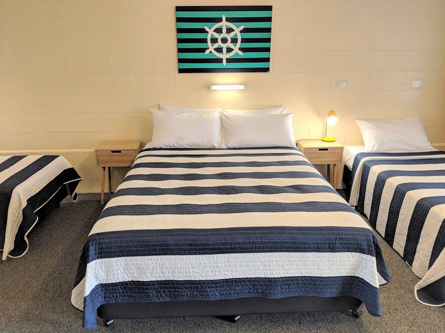 Una habitación de hotel con una cama grande, dos mesitas de noche, una obra de arte en la pared y suelo alfombrado.