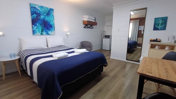A hotel room with a bed, a desk, a chair, a mirror, and a small kitchenette.