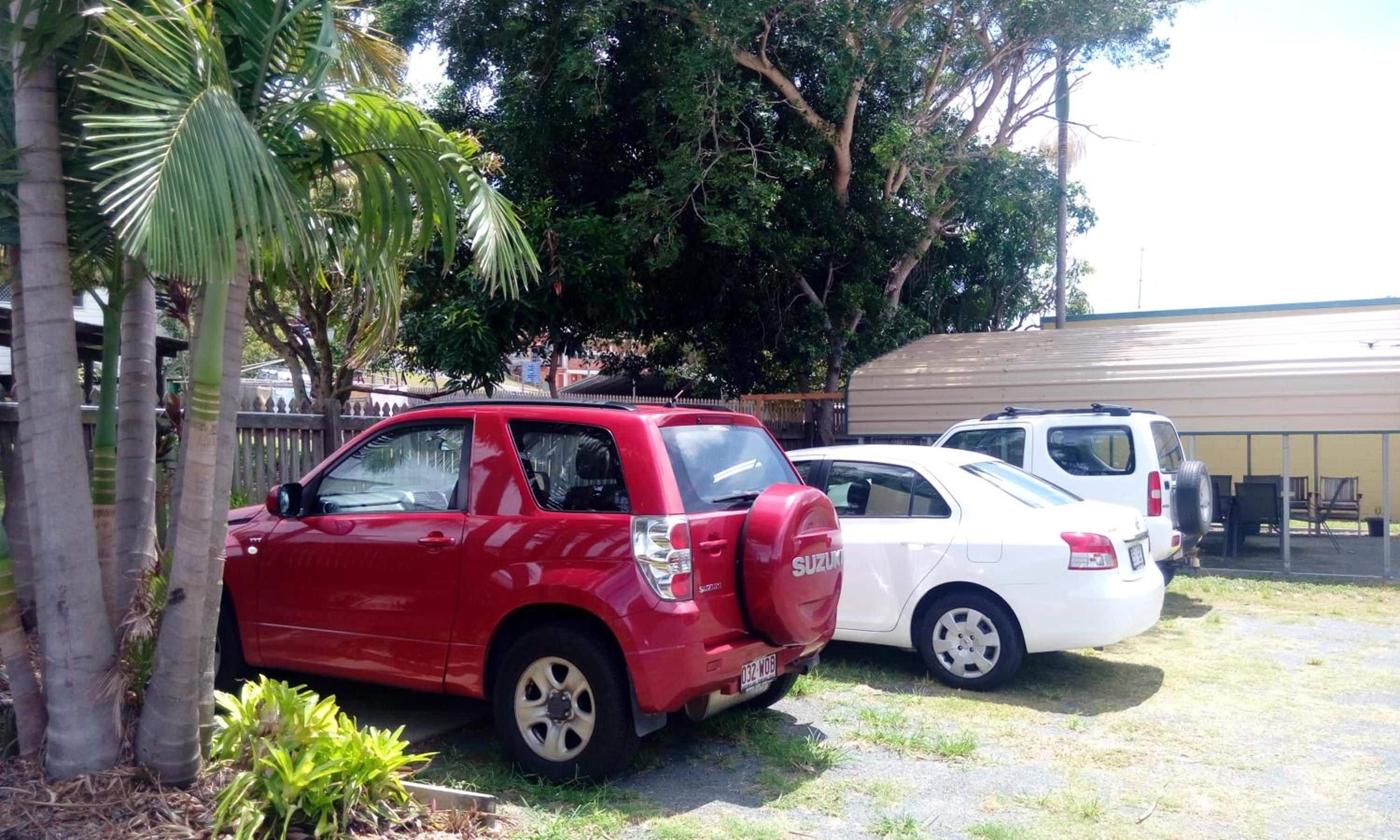 A red SUV and a white car parked in a lot with a building in the background.