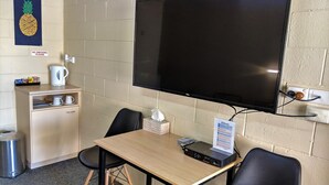 Una habitación pequeña con televisor, una mesa, dos sillas, una cafetera y un cubo de basura.