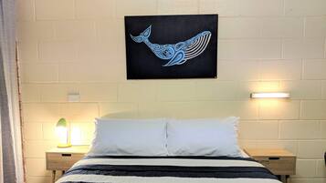 A bed with a striped bedspread, two white pillows, and a wall-mounted artwork of a blue whale. There are two bedside tables with lamps, and a white brick wall.