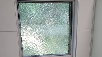 Un baño pequeño y limpio con inodoro, un cesto de basura y una ventana sobre el inodoro.