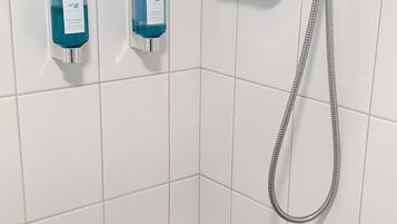 A shower with a handheld showerhead and a handheld hose, two soap dispensers, and a wall-mounted faucet.