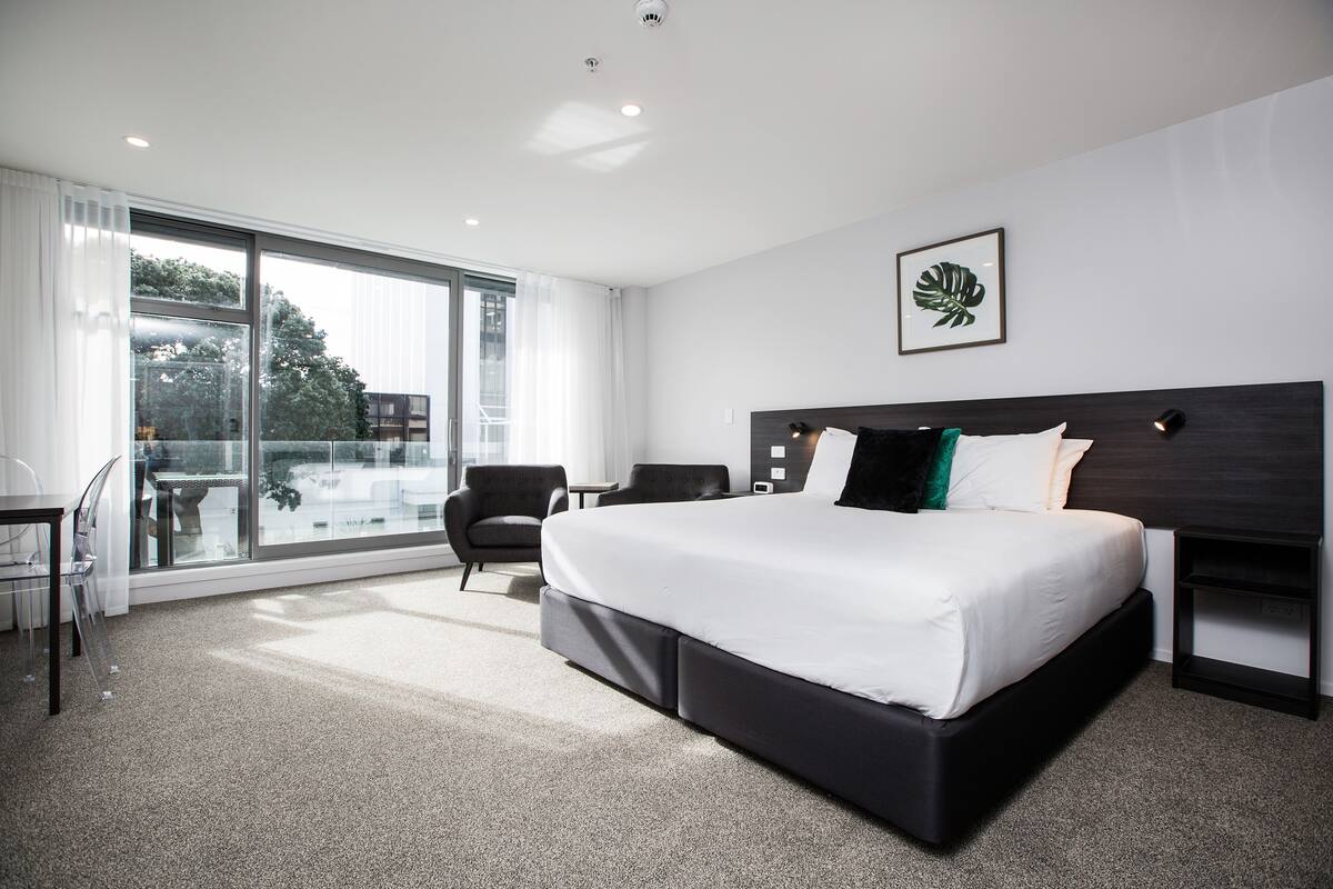 A modern hotel room with a large bed, a desk, and a chair.