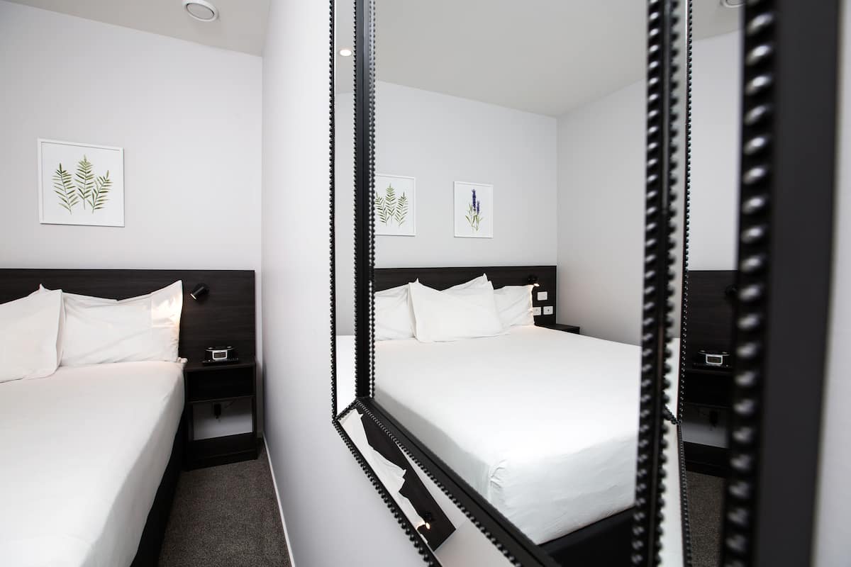 A modern hotel room with a large bed, a nightstand, and a mirror reflecting the room.