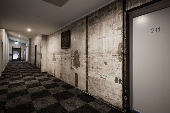 Un pasillo con piso de cuadros, una puerta con la etiqueta 211 y una pared con pintura descascarada.