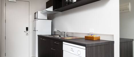 A compact kitchen with dark wood cabinets, a white dishwasher, and a built-in microwave.