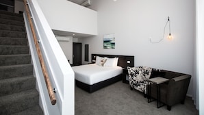 Een moderne slaapkamer met een groot bed, een bureau, een stoel en een trap.