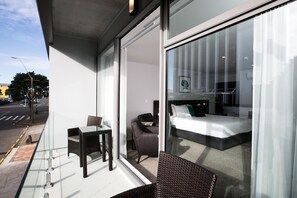 Habitación de hotel moderna con pared de vidrio, cama, sillón y una mesita.