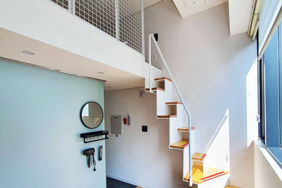 Un interior moderno con suelo de madera, una escalera con peldaños de madera, una pared blanca y una ventana.
