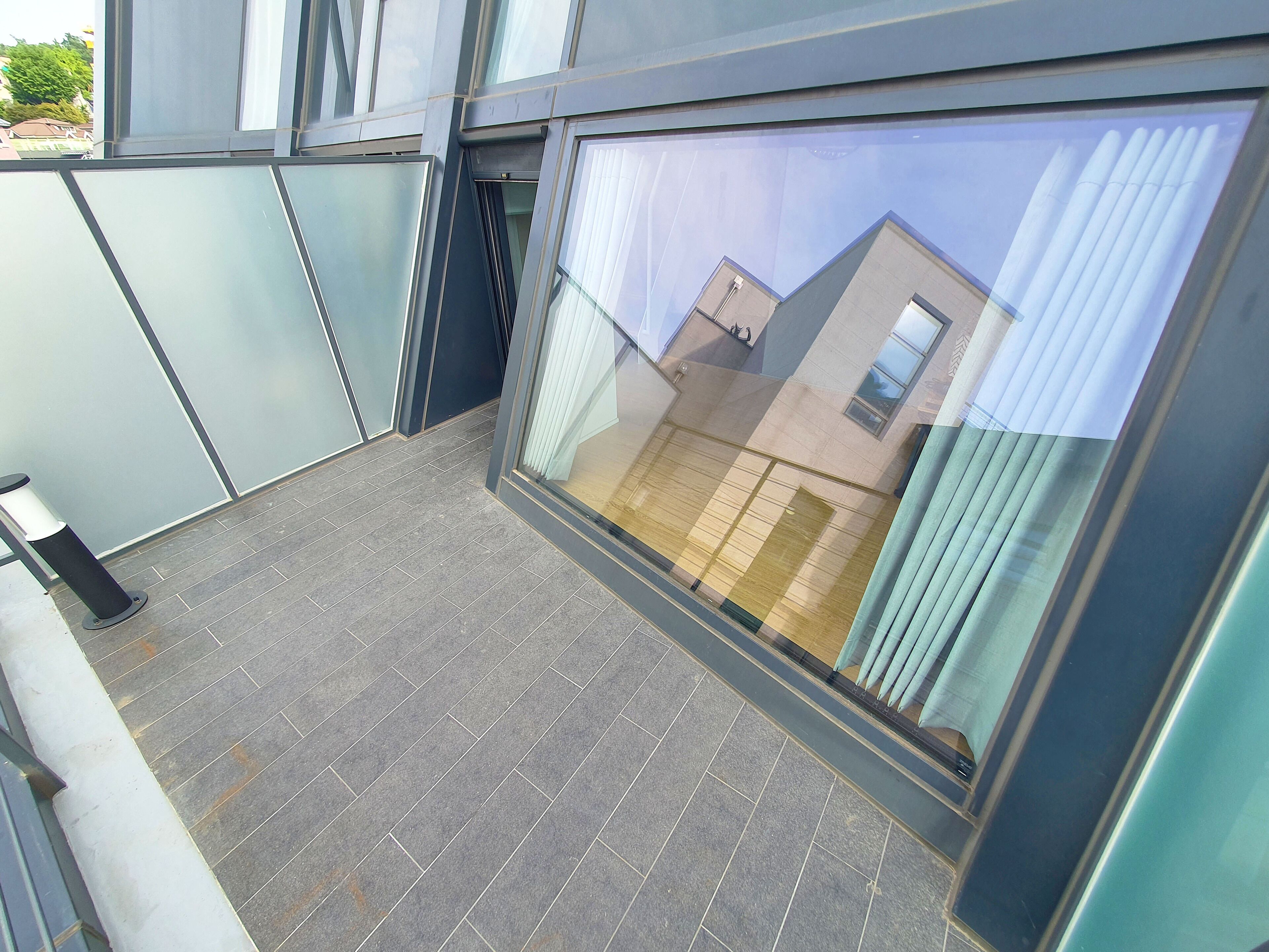 A modern building with a balcony featuring grey tiled flooring and large windows.