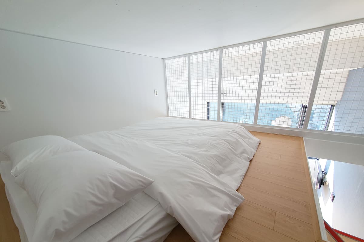 Un dormitorio con una cama grande, piso de madera y vistas a través de una ventana con diseño de cuadrícula.
