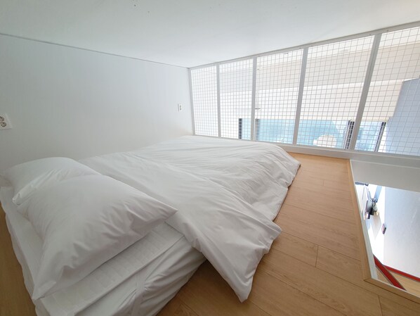 A bedroom with a large bed, a wooden floor, and a view through a window with a grid pattern.