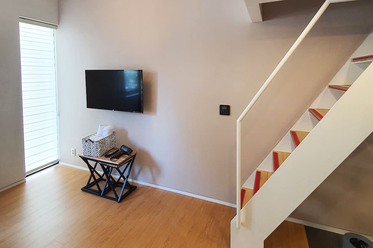 Una sala de estar moderna con un televisor de pantalla plana montado en la pared, suelo de madera y una escalera con barandilla blanca.