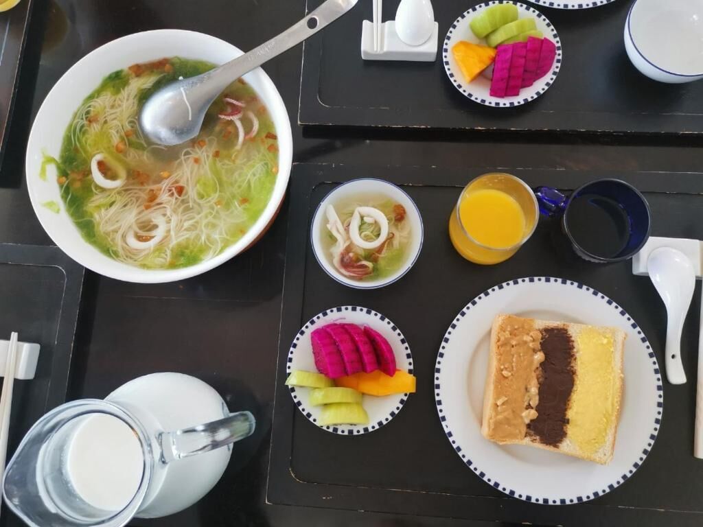 A table with a bowl of soup, a small bowl of pickled vegetables, a plate of colorful vegetables, a glass of orange juice, a cup of milk, and a slice of cake.